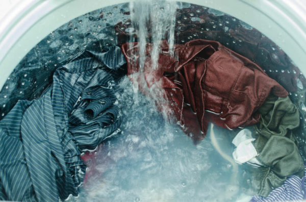 Close-up view of clothes being washed in a washing machine, with water pouring over various colored garments.