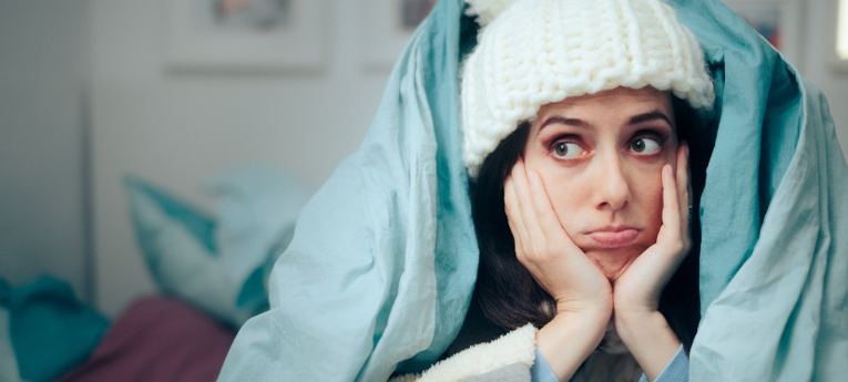 %Title% | Sal'S Heating &Amp; Cooling, Plumbing &Amp; Sewer A woman wearing a white knit hat sits with her hands on her cheeks, wrapped in a blue blanket, looking to the side with a bored or tired expression.