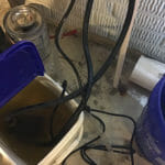 %Imagetitle% | Sal'S Heating &Amp; Cooling, Plumbing &Amp; Sewer A plastic bucket filled with murky water, black hoses, and electrical cords on a concrete floor in a utility area.