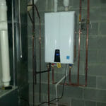 %Imagetitle% | Sal'S Heating &Amp; Cooling, Plumbing &Amp; Sewer A wall-mounted tankless water heater with copper piping is installed in a basement with concrete block walls.