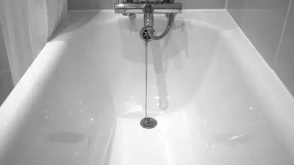 A clean, empty white bathtub with a metal drain stopper attached to a chain and a silver faucet above.