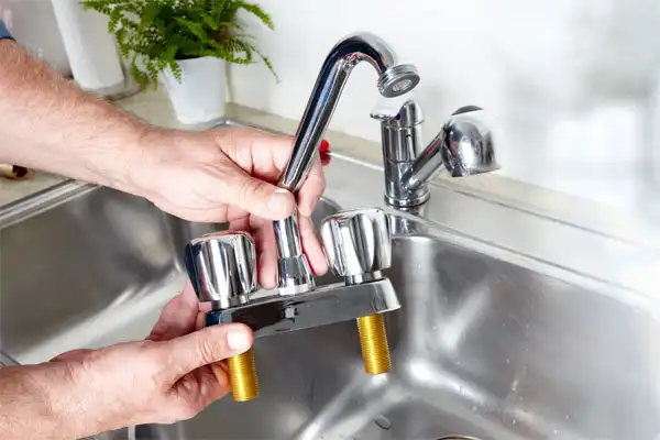 A person holds a two-handle kitchen faucet over a sink, preparing to install or replace it.