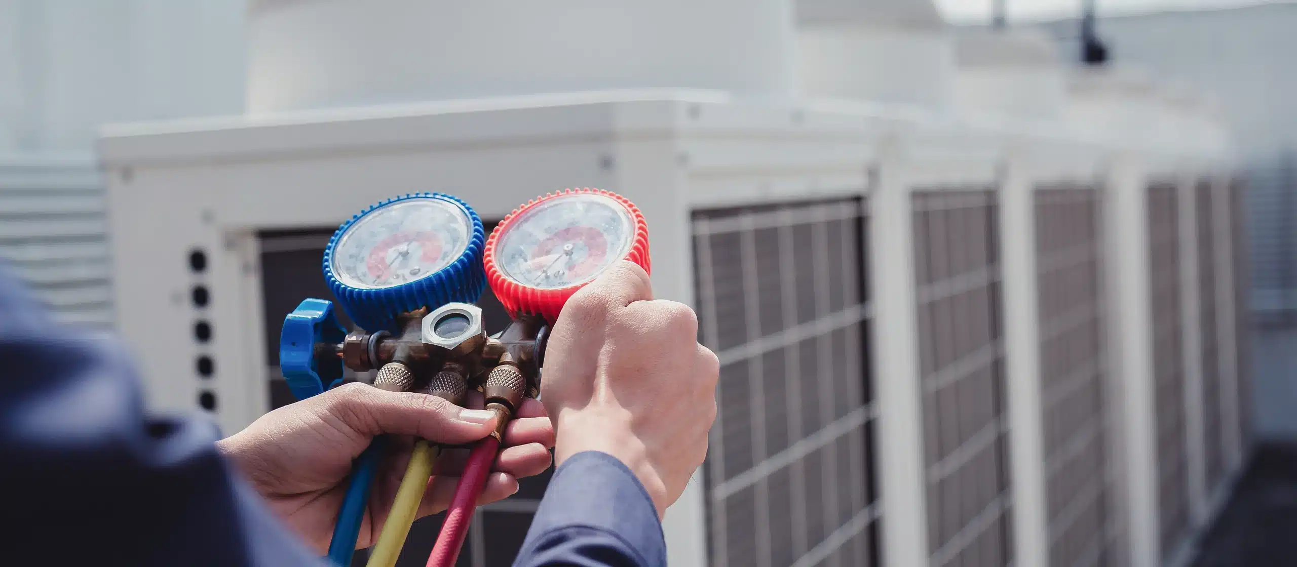 A person uses HVAC manifold gauges to check the pressure on rooftop air conditioning units.