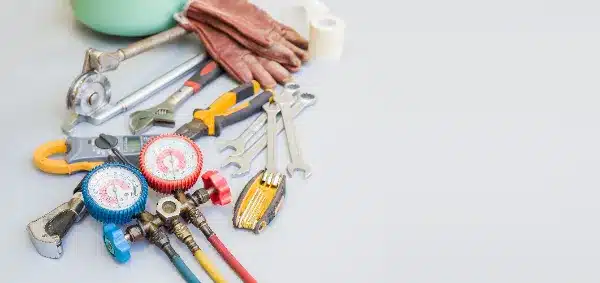 Assorted plumbing tools, pipe wrenches, gauges, wrenches, pliers, gloves, and tape arranged on a light surface.