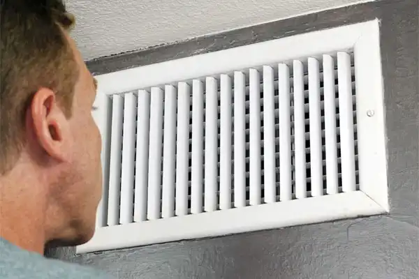 A person closely inspecting a white wall-mounted air vent.