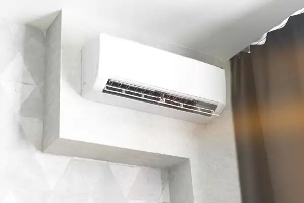 A wall-mounted air conditioning unit is installed near the ceiling in a modern room with light-colored walls and a dark curtain.