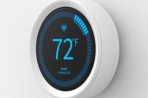A round smart thermostat mounted on a wall displays a temperature of 72°F with a Wi-Fi symbol and a blue progress bar around the screen.