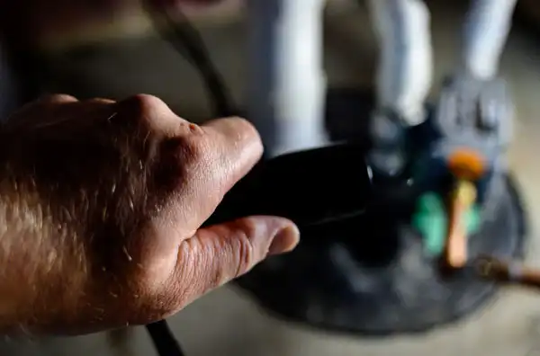 A close-up of a hand holding a black object near blurred machinery and pipes in the background.