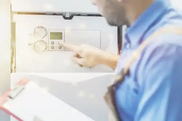 A technician in a blue shirt adjusts the settings on a control panel, holding a clipboard while inspecting equipment.