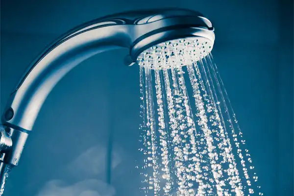 A close-up of a showerhead with water spraying out, set against a blue-toned background.