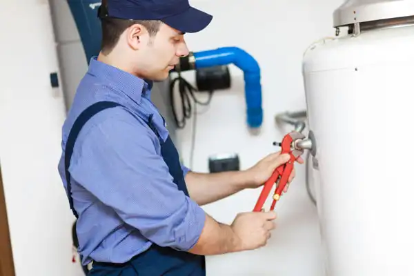 A plumber in uniform uses a pipe wrench to work on a water heater.