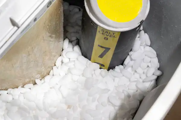 Water softener tank filled with salt pellets, showing a yellow indicator marked with the salt level.