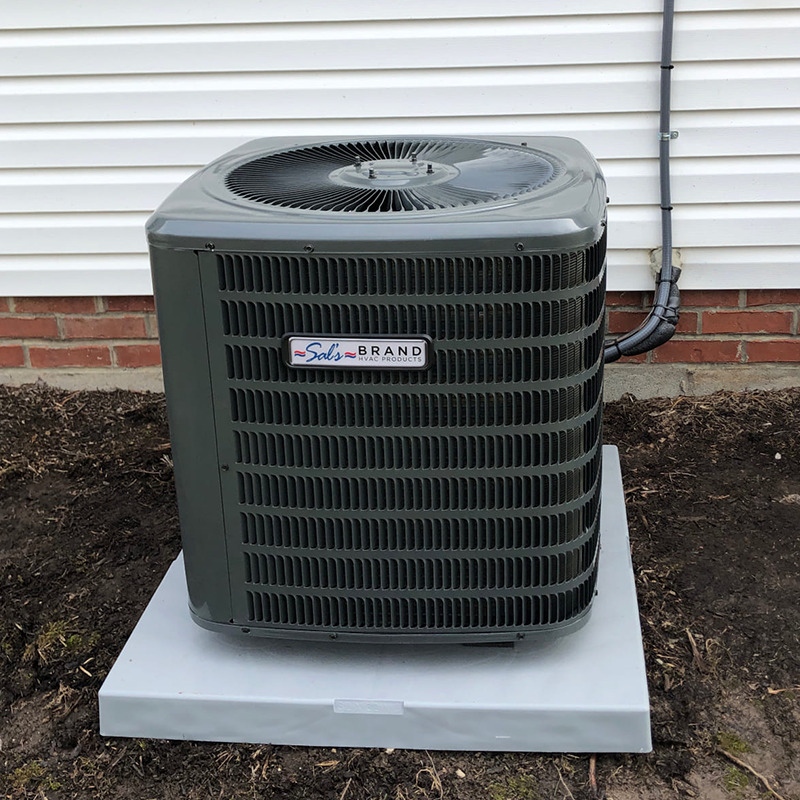 A central air conditioning unit labeled "Sol's Brand" is installed outdoors on a concrete pad next to a house with white siding and red brick.